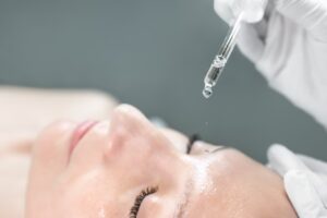 Close-up beautician doctor hand in protection gloves making anti-age procedure applying serum